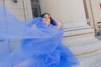 a woman in a blue tulle dress leaning against a column