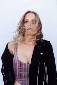 a woman in a black jacket posing in front of a white wall