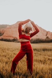 a woman in a red crop top and pants standing in a field
