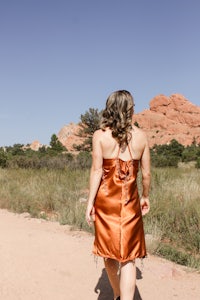 a woman walking down a dirt road in an orange dress